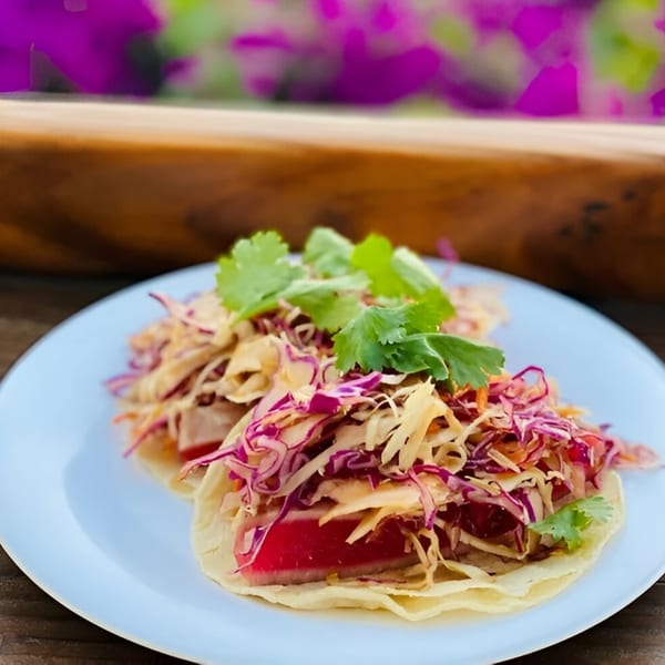 Two vibrant fish tacos with red cabbage slaw and cilantro on a light blue plate.