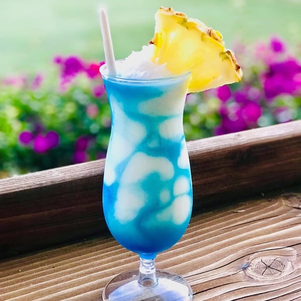 A blue and white swirled frozen drink with a pineapple slice and straw on a wooden railing.
