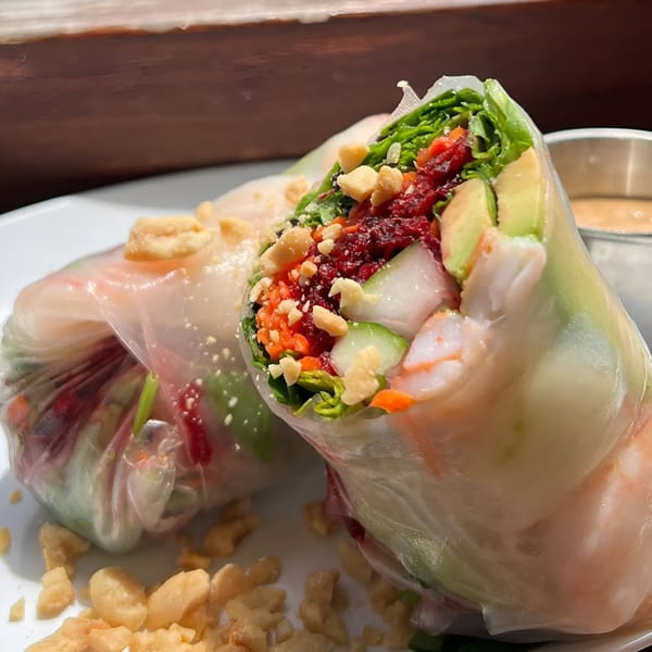 Two fresh spring rolls filled with shrimp, avocado, vegetables, and peanuts, served with dipping sauce.