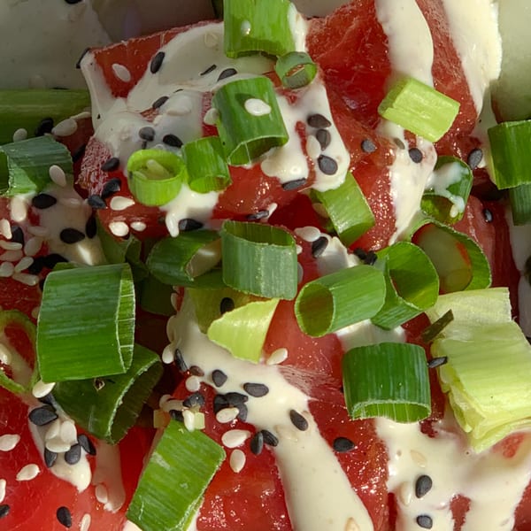 Close-up of red tuna poke with white sauce, green onions, and sesame seeds.