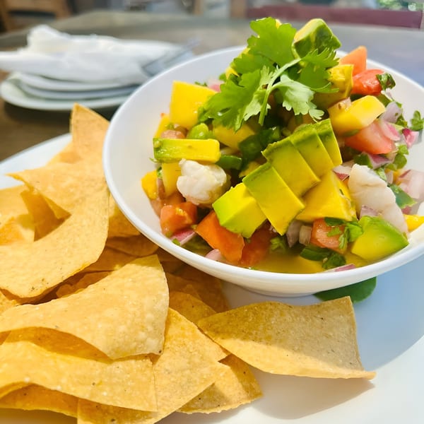 A white bowl of colorful ceviche with avocado, mango, and cilantro, served with tortilla chips.